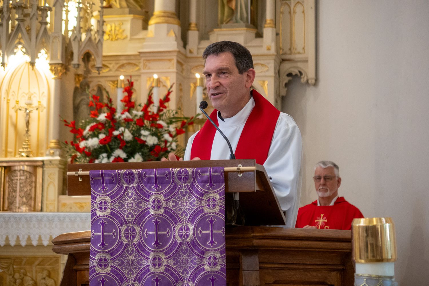 Religious service taking place inside ornate church with gold decorations and purple altar cloths.