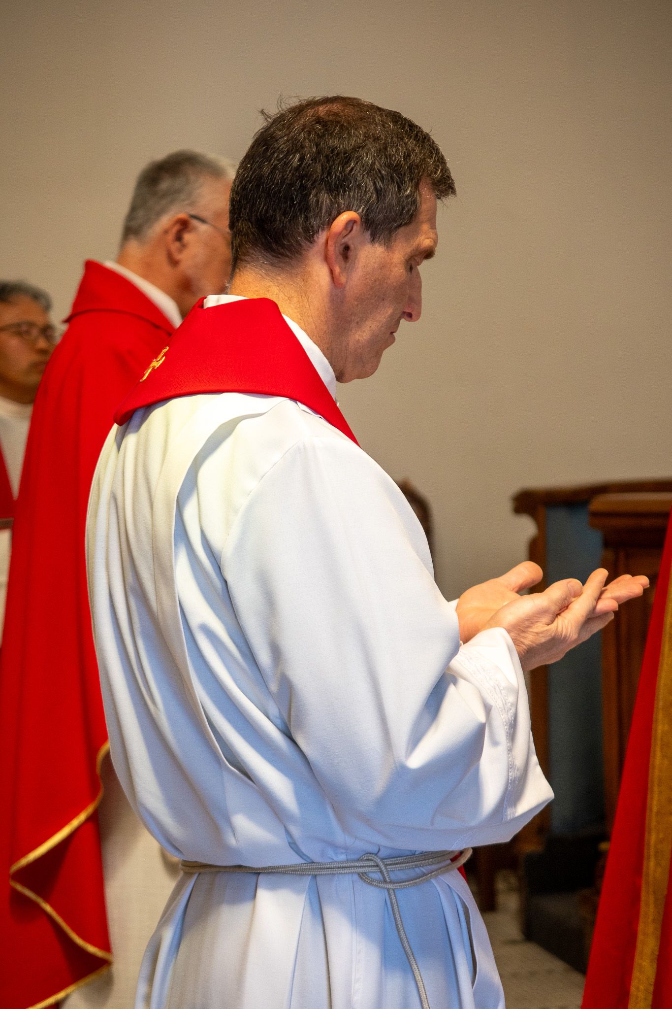 Side view of clergy members in white and red vestments during a religious service in church.