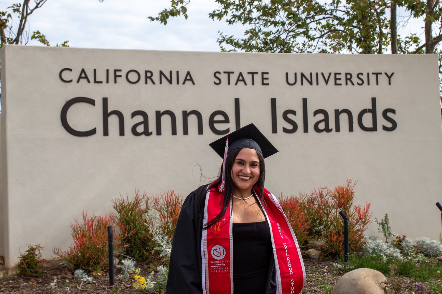 Graduates in black caps and gowns with red stoles celebrate during an outdoor commencement ceremony at California State University.