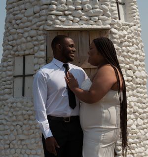 A couple in formal attire embraces against a white stone wall background.