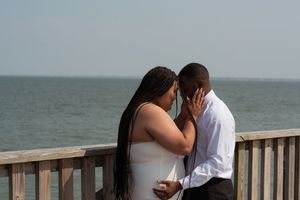 A couple shares a romantic kiss standing together on a wooden pier overlooking the ocean on a cloudy day.