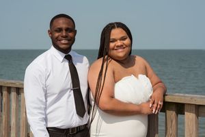 A couple poses for romantic beach photos in white attire with ocean backdrop.