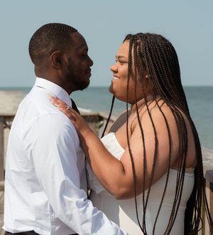 Romantic couple in white attire sharing an intimate moment at a beach with ocean in background.