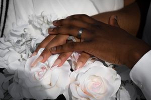 Close-up details of delicate white roses and hands with rings.