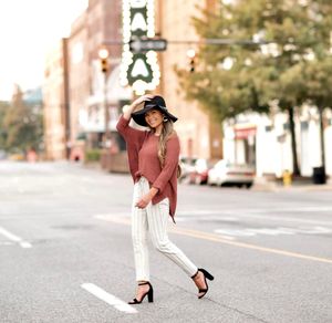 Stylish outfit featuring a dusty rose sweater paired with white pants and black heels on a quiet city street.