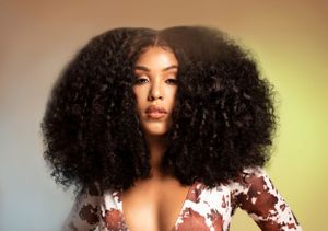 Portrait photo of a woman with voluminous natural curly hair wearing floral print against warm-toned background for Afromeplease.