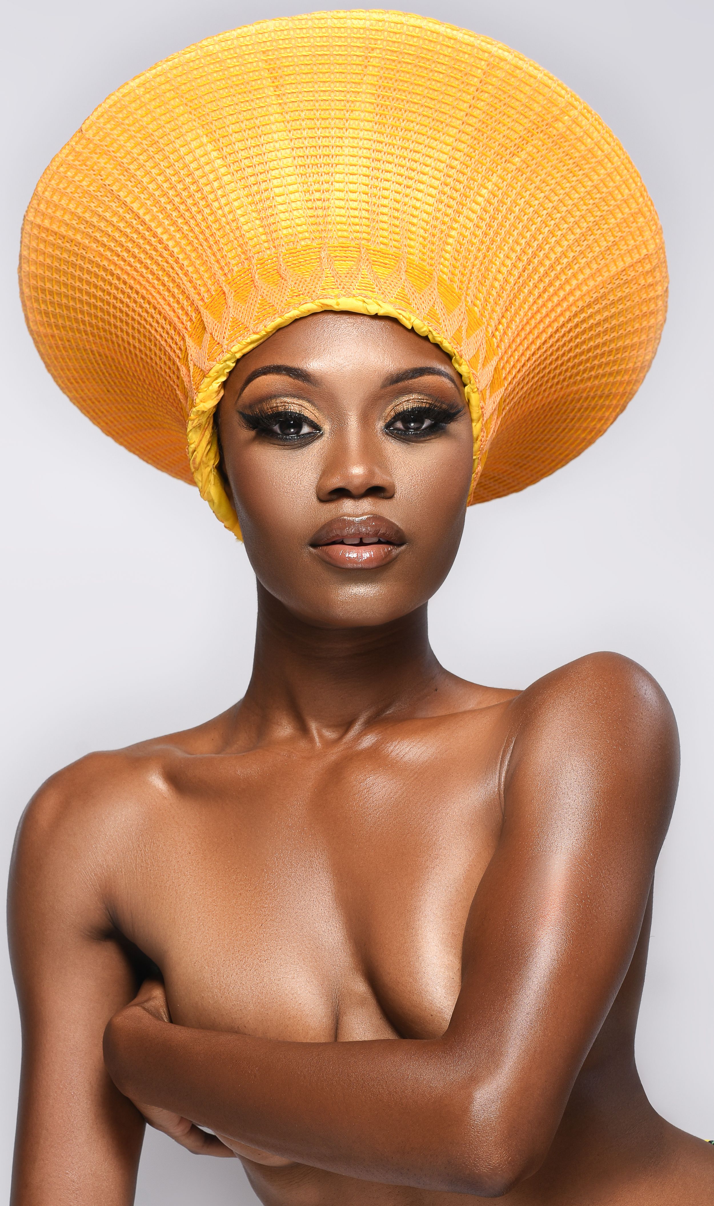 Fashion portrait with striking large yellow circular headpiece against white background.
