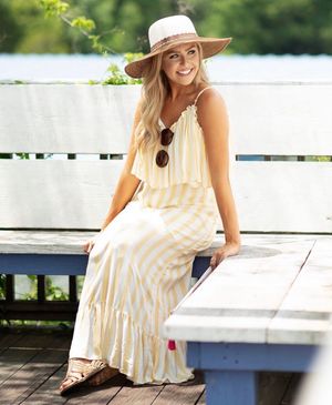 A summery scene on a deck with a flowy cream maxi dress, sunhat and sunglasses creating a relaxed coastal look.