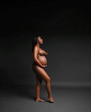 Artistic nude maternity portrait of an expectant mother in a minimalist dark studio setting.
