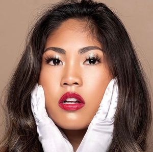 Beauty portrait with red lipstick and white gloves showing glamorous makeup against beige background.