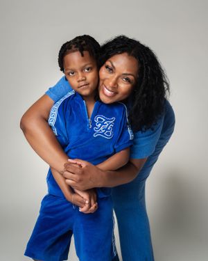 A parent and child wearing matching royal blue outfits share a loving embrace against a neutral background.