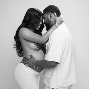 Black and white intimate portrait of an expecting couple embracing tenderly against a plain wall.