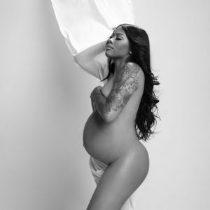 Artistic black and white maternity photo of nude pregnant figure draped in flowing white fabric.