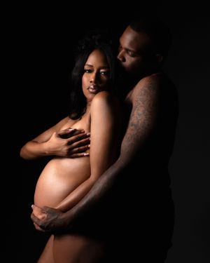 Intimate maternity portrait of a couple embracing in dramatic low-key lighting against a dark background.