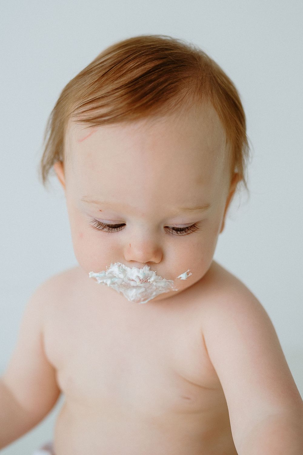 Close-up portrait of a baby with frosting smeared around mouth after eating birthday cake.