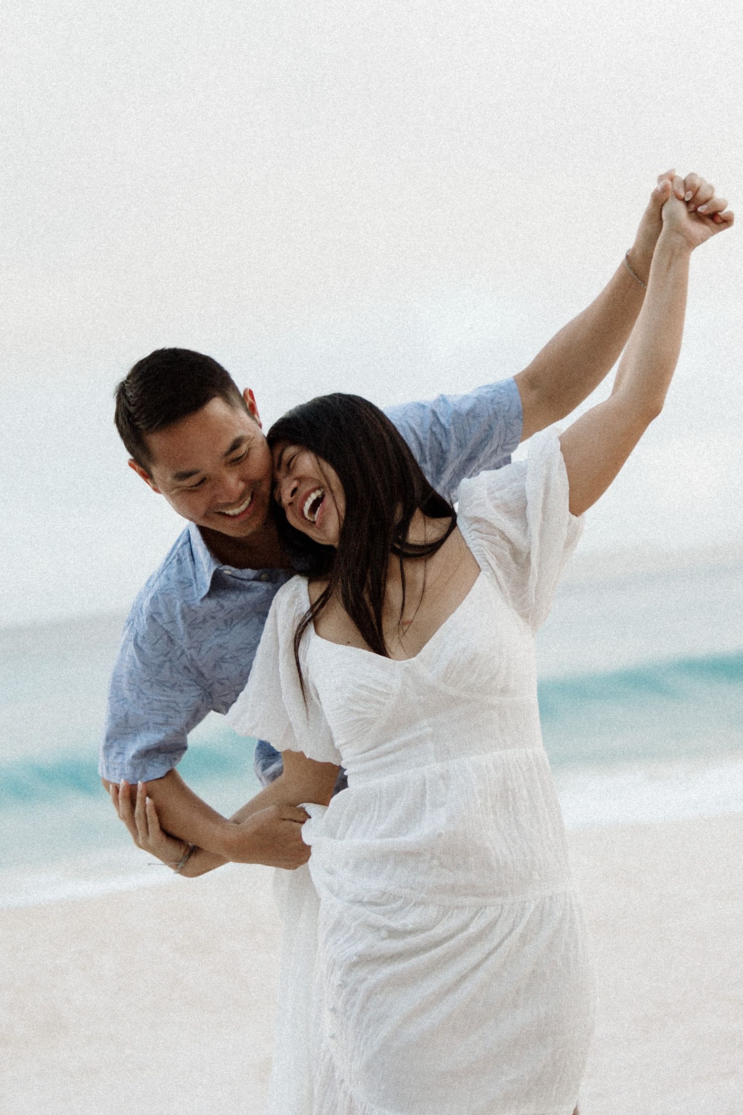 A joyful moment captured on a white sandy beach with ocean waves in the background.