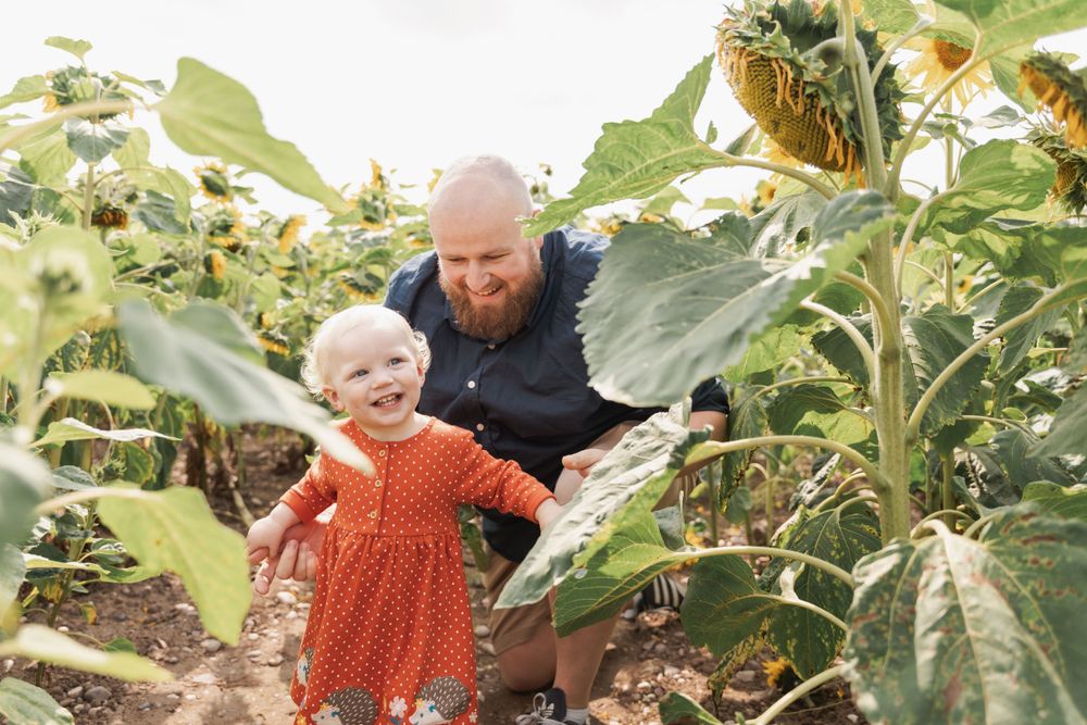 Parent and child explore a garden filled with towering sunflower plants.