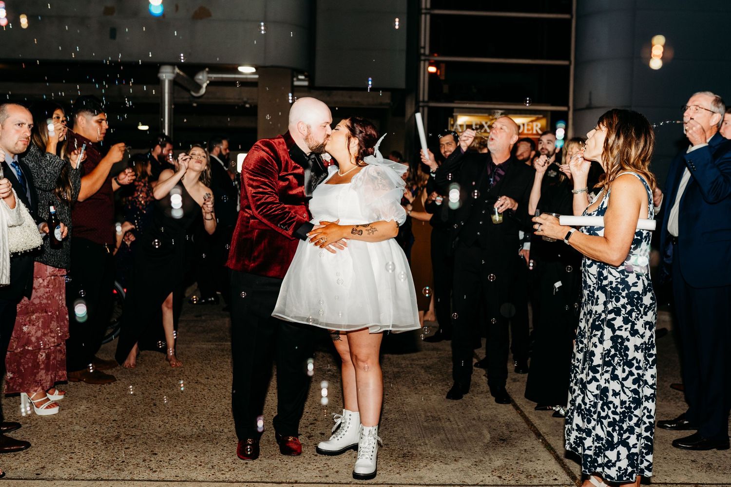 Two people dancing at a reception while guests look on and take photos in a dark venue space.