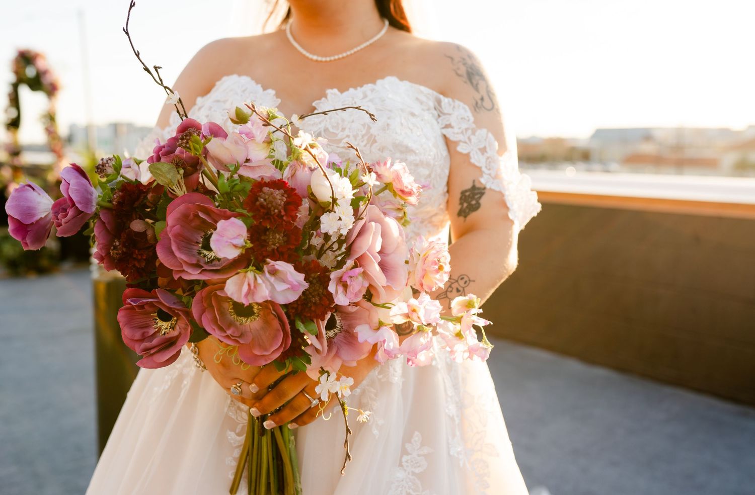 A bride holding a lush pink and orange bouquet with orchids and roses against a waterfront backdrop.