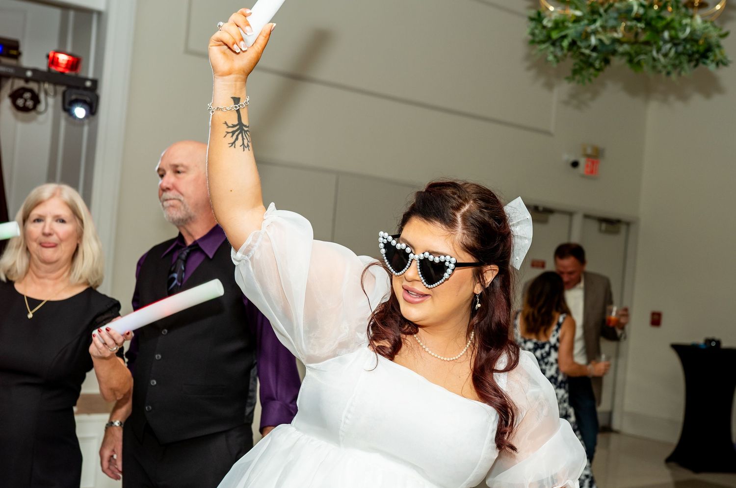 A person in a white wedding dress raises their hand in celebration while dancing at an indoor reception.