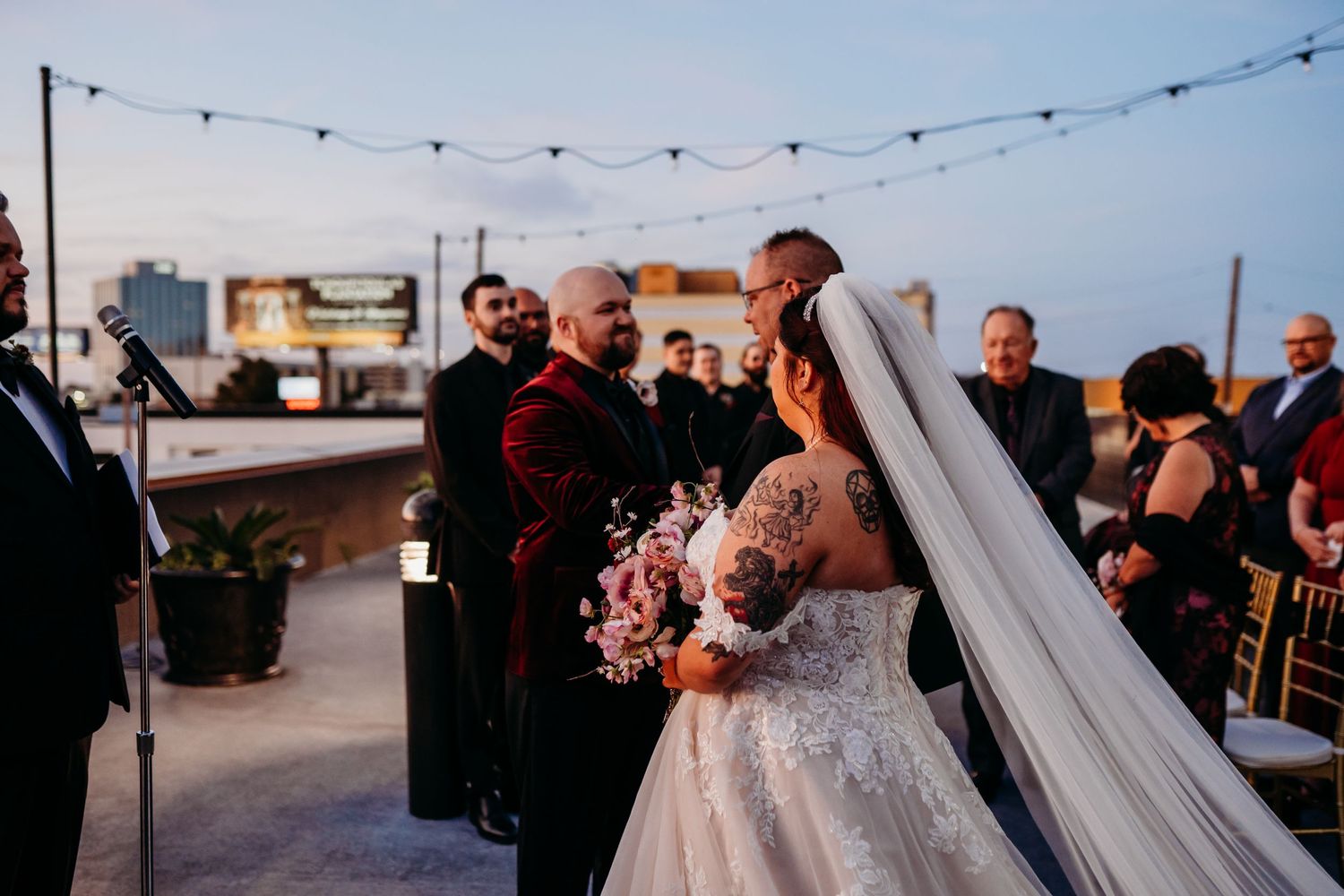 A joyful moment at a rooftop wedding ceremony with string lights and city views at dusk.
