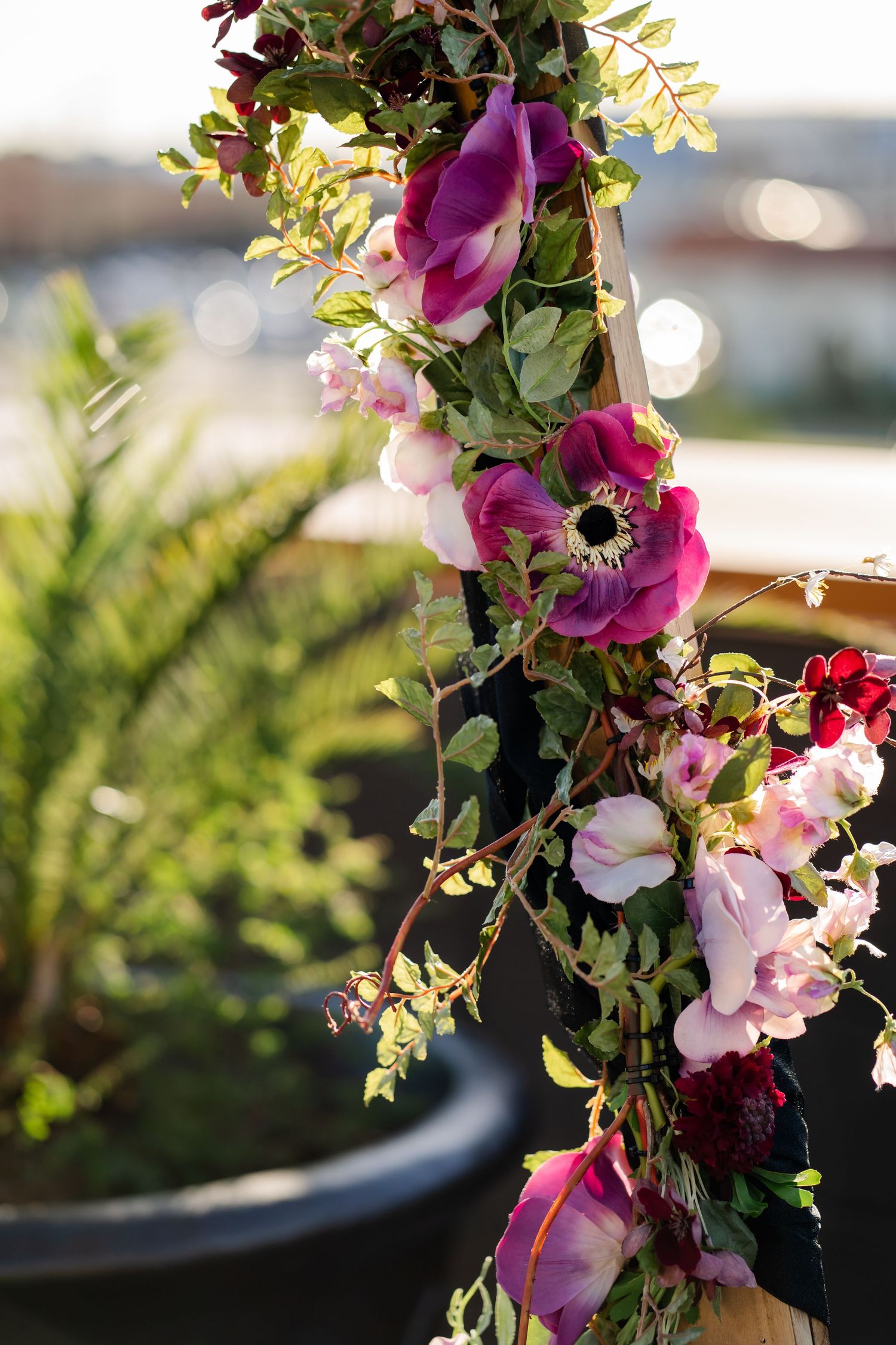 A beautiful floral arrangement featuring pink and purple anemones, roses, and delicate green foliage in soft sunlight.