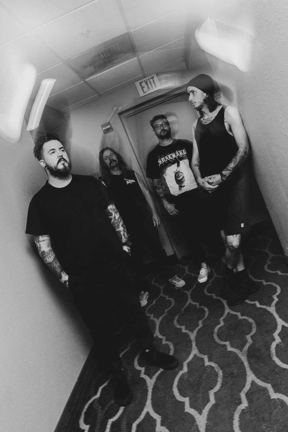 Black and white photo of four tattooed rock band members posing in a dimly lit hotel hallway.