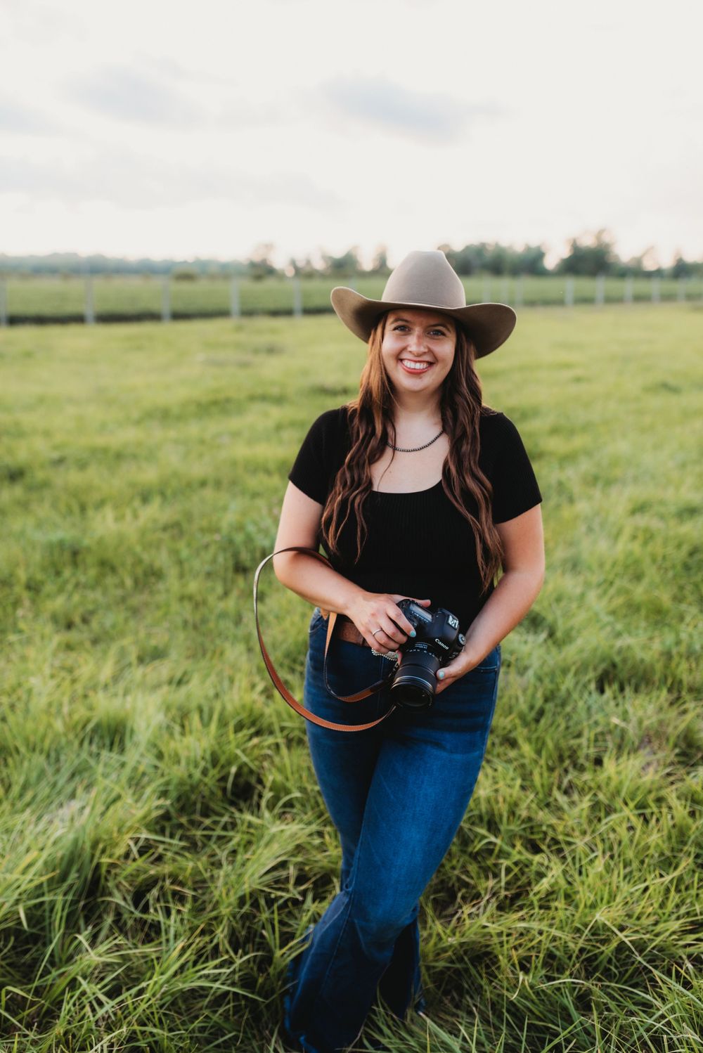Person wearing a cowboy hat poses in a sunlit grassy field.