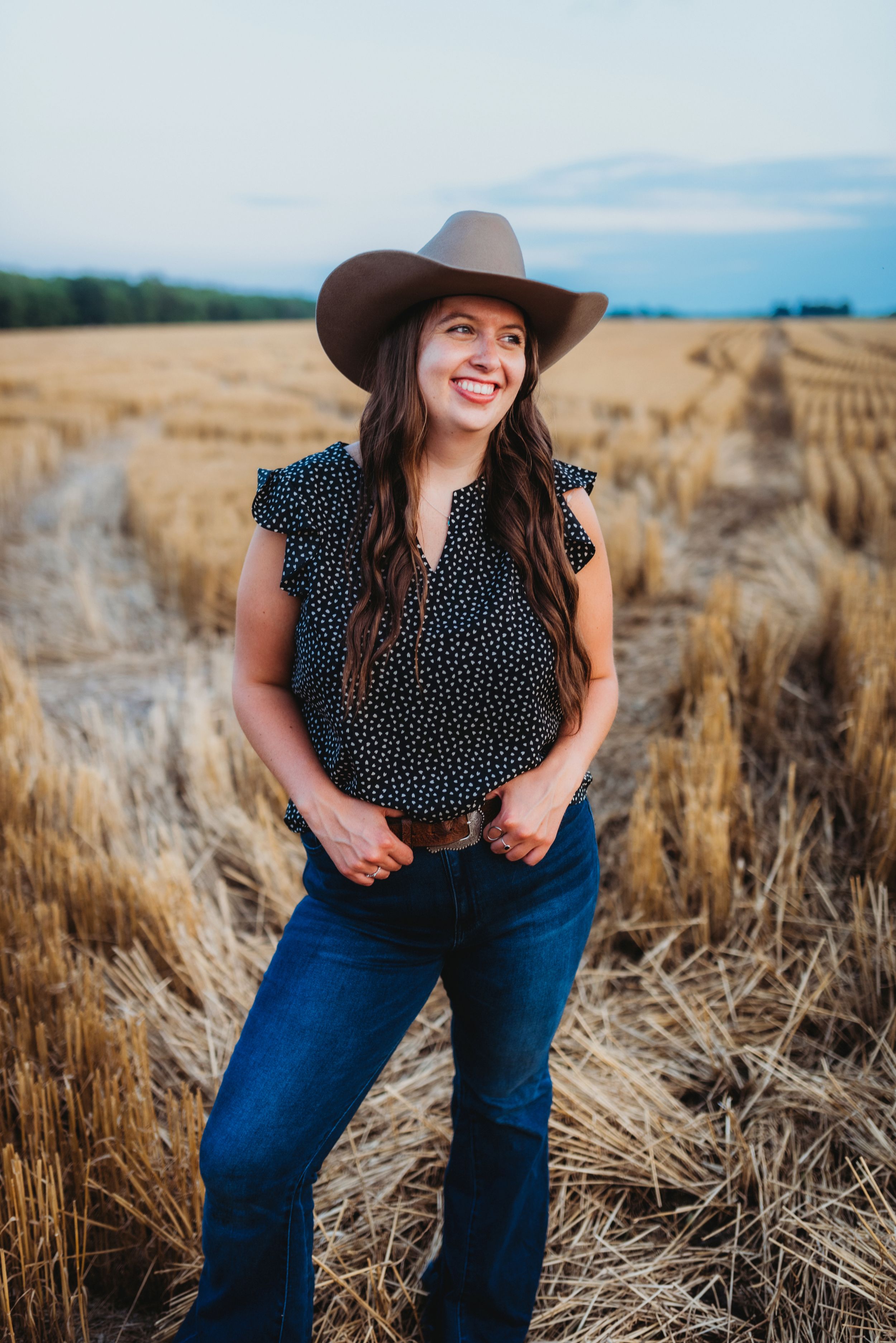 Person in polka dot top and cowboy hat poses in a golden wheat field.