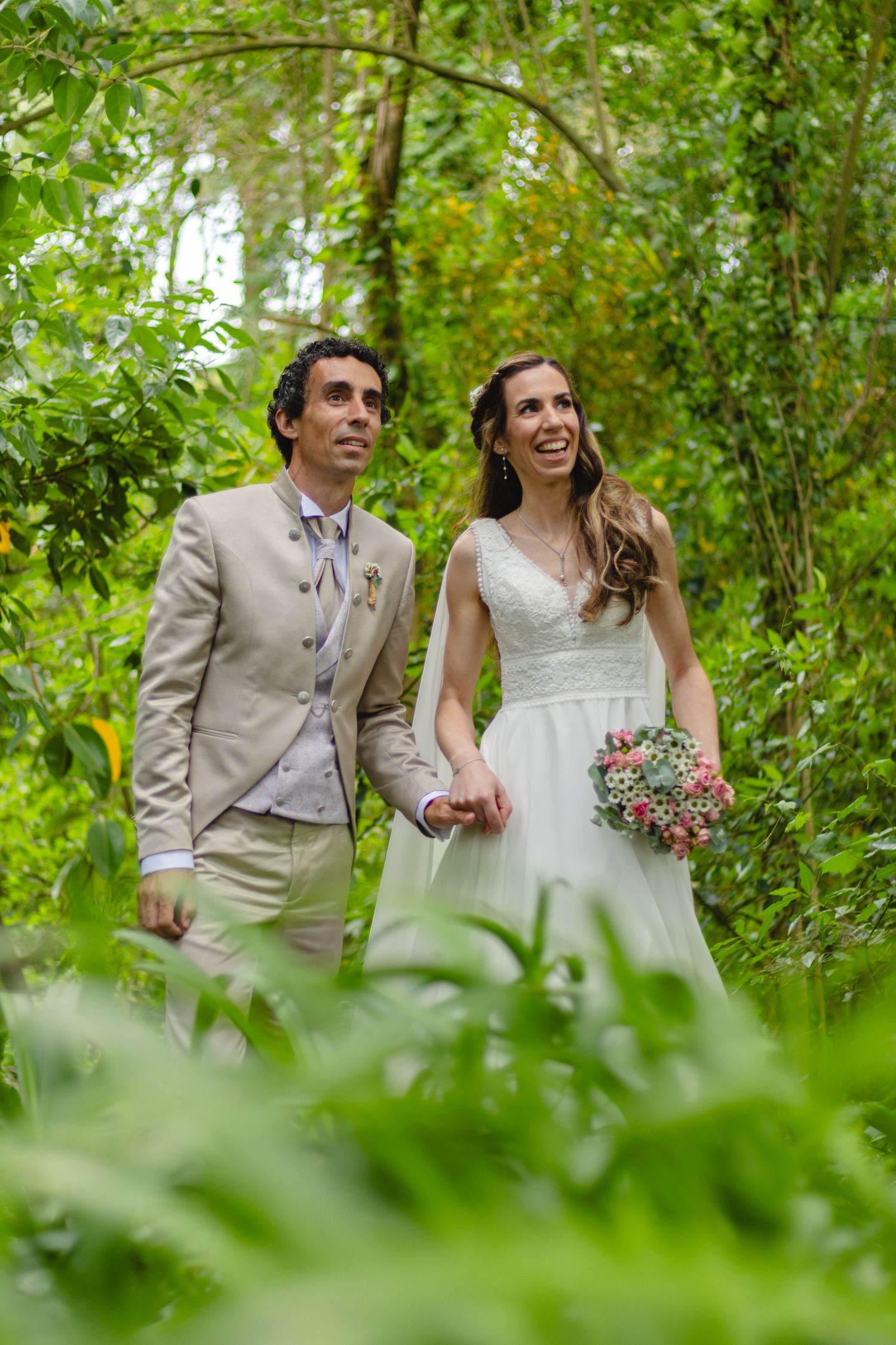 Newlyweds walking and laughing together through lush green foliage.