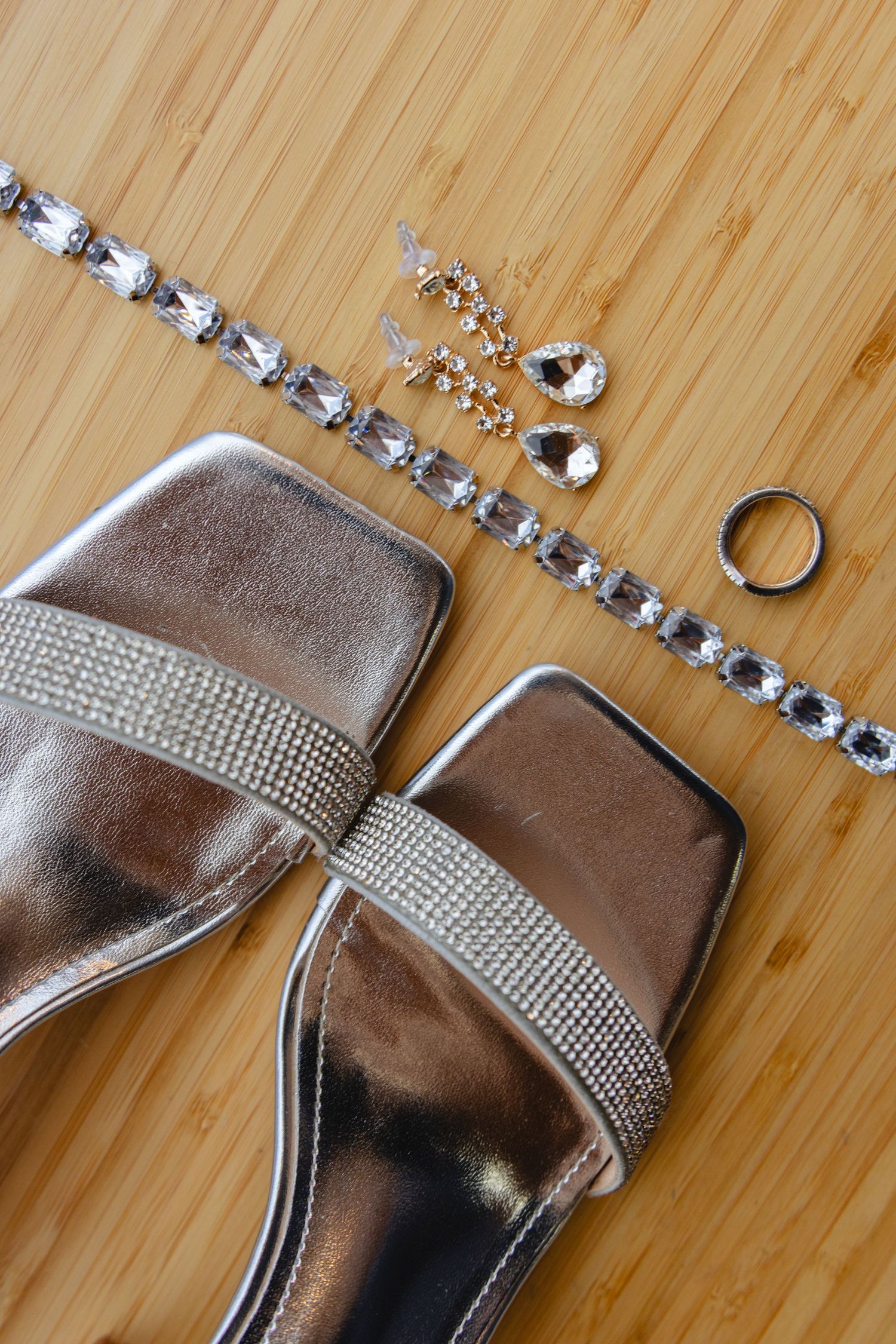 Silver wedding accessories and jewelry arranged on a wooden surface.