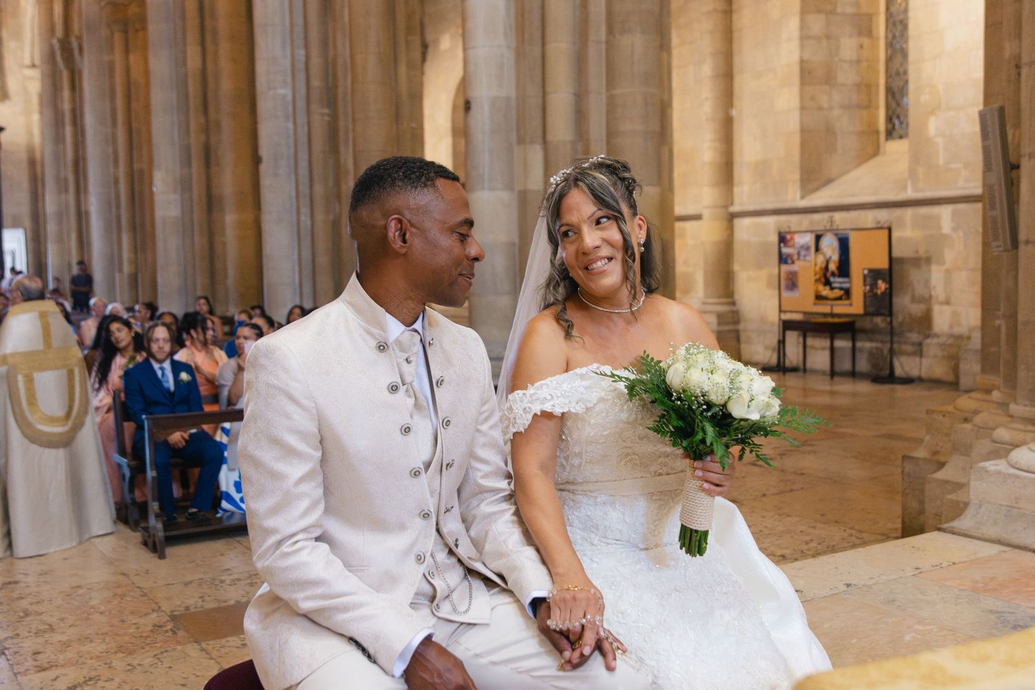 Wedding couple seated in elegant stone church interior with classic architecture.