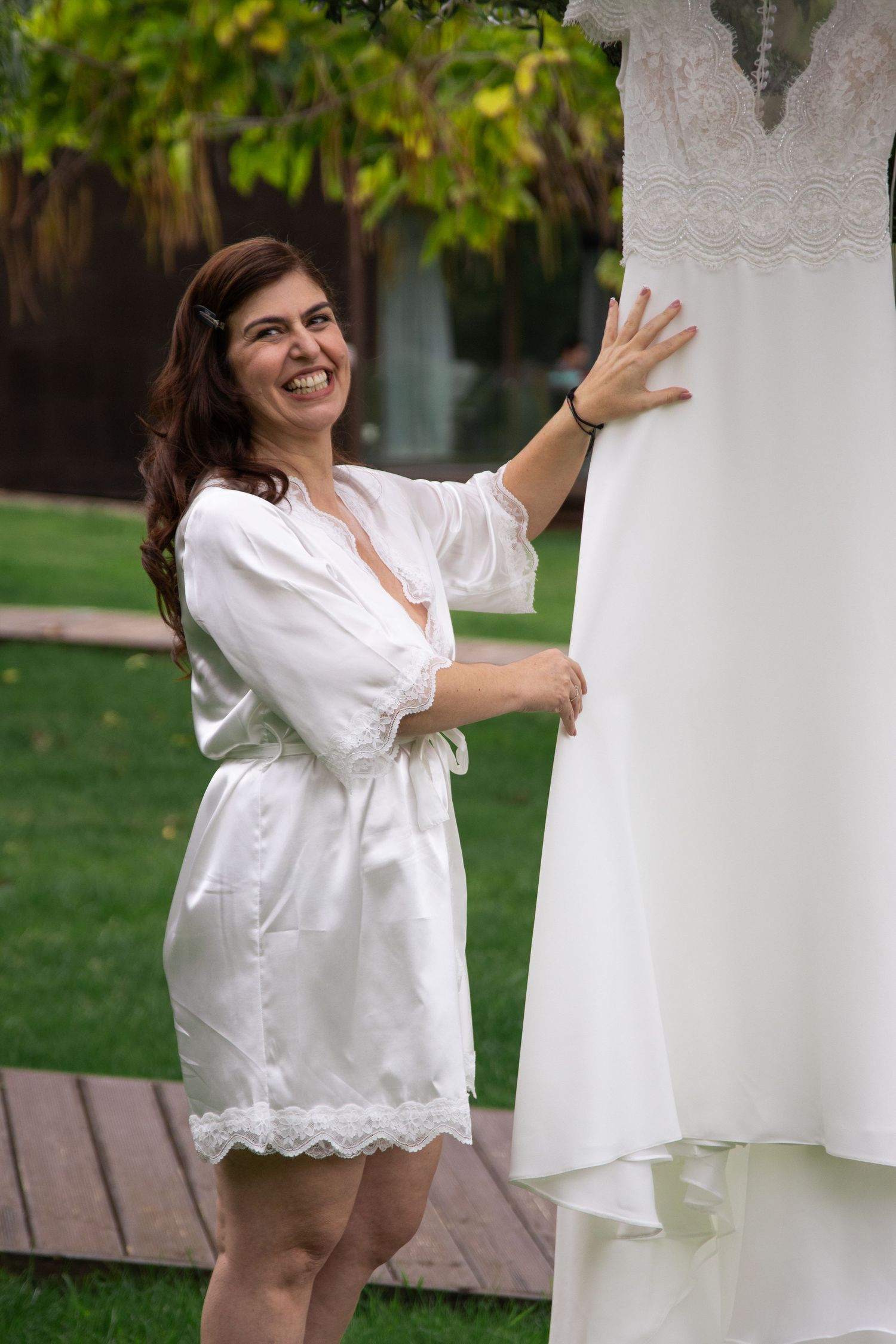 A person in white attire poses with a wedding dress in a garden setting.