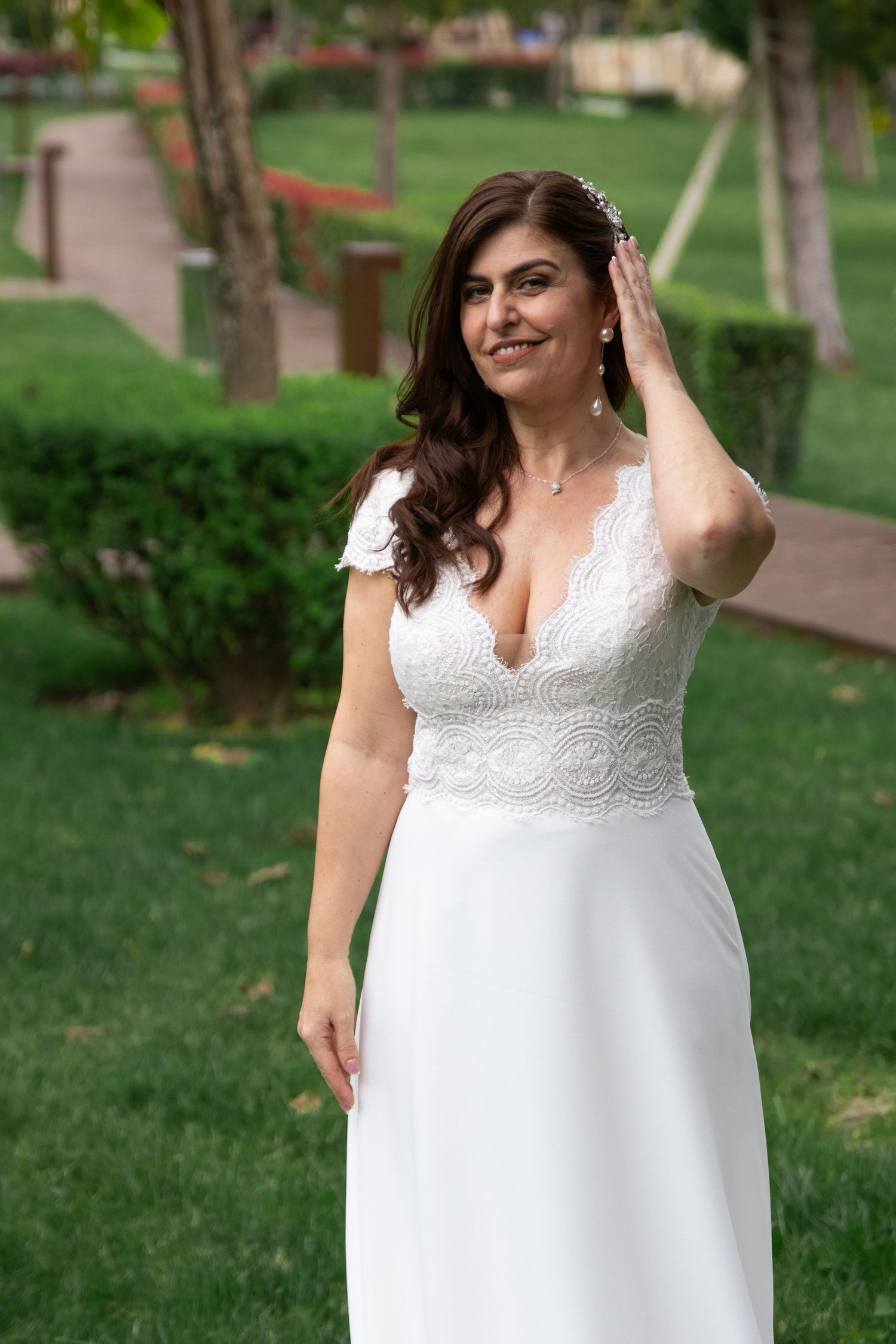 A bride in a white lace dress poses gracefully in a garden setting.