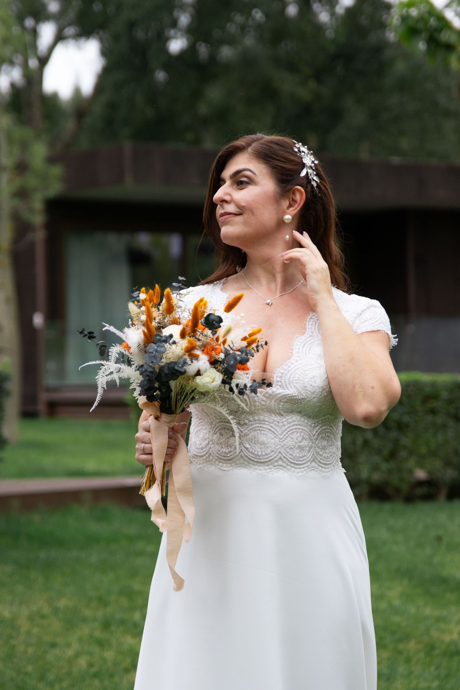 A bride in a cap sleeve wedding gown holds a vibrant orange and white floral bouquet outdoors.