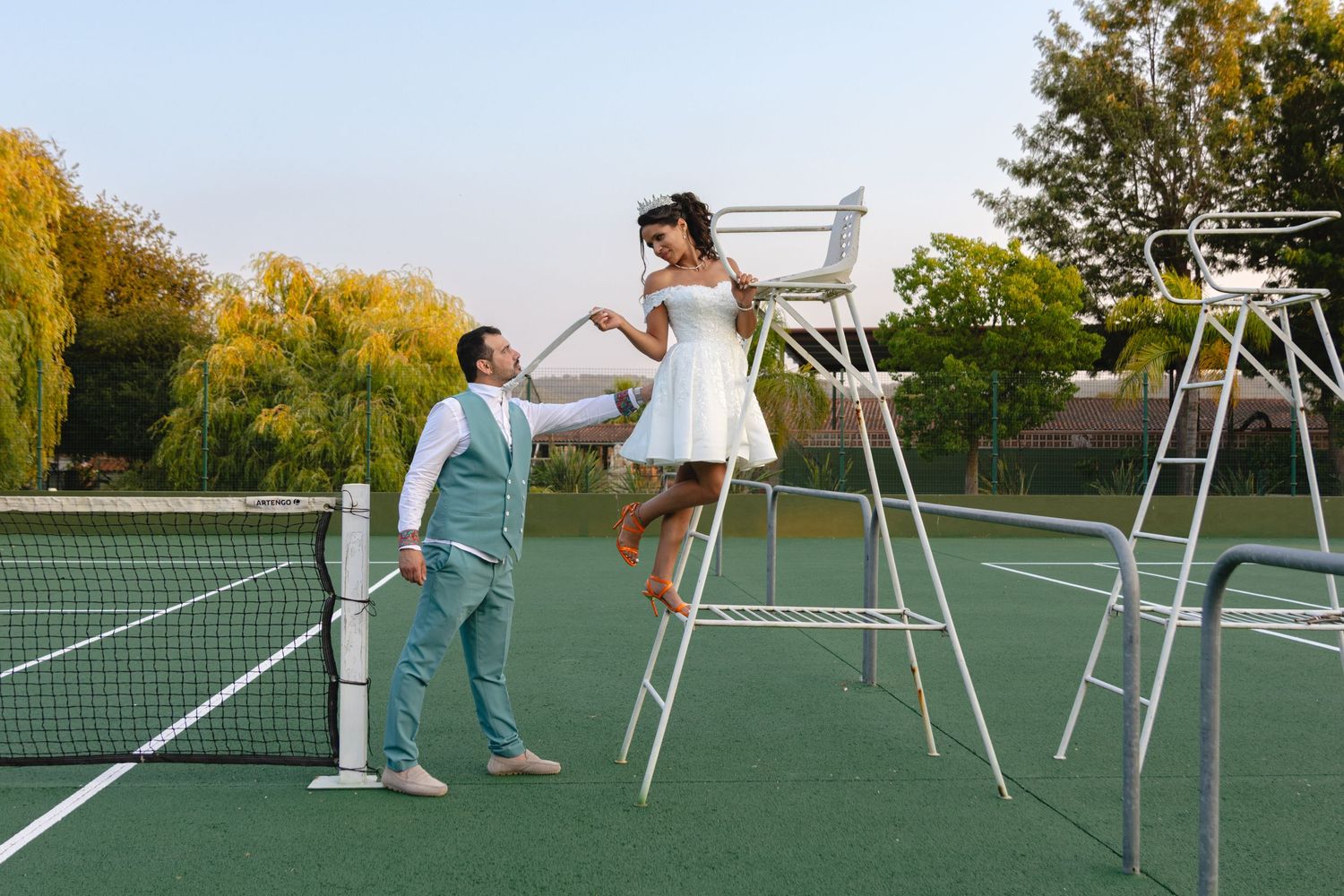 Creative wedding photography on a tennis court with white chairs.