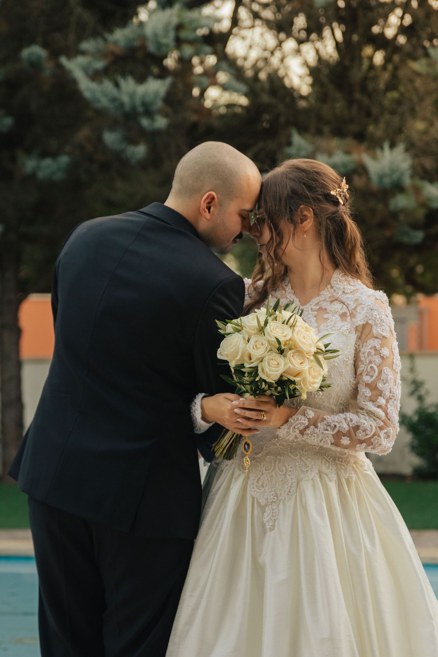 Romantic wedding couple shares intimate moments in an outdoor garden setting with white floral bouquet.