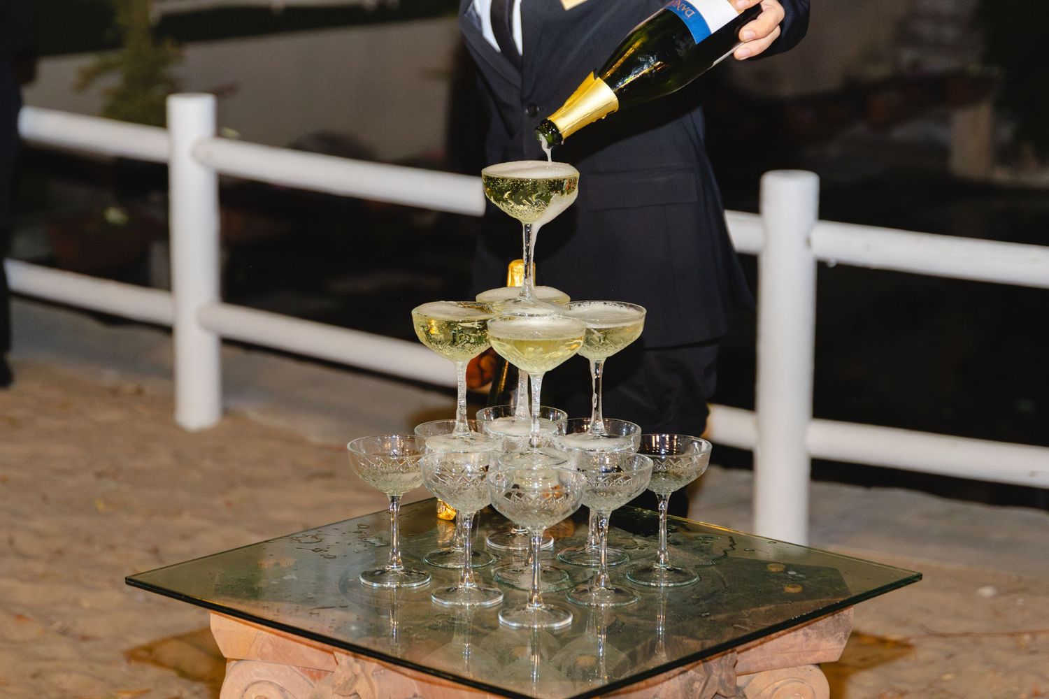 Champagne tower being poured at an elegant outdoor wedding reception.