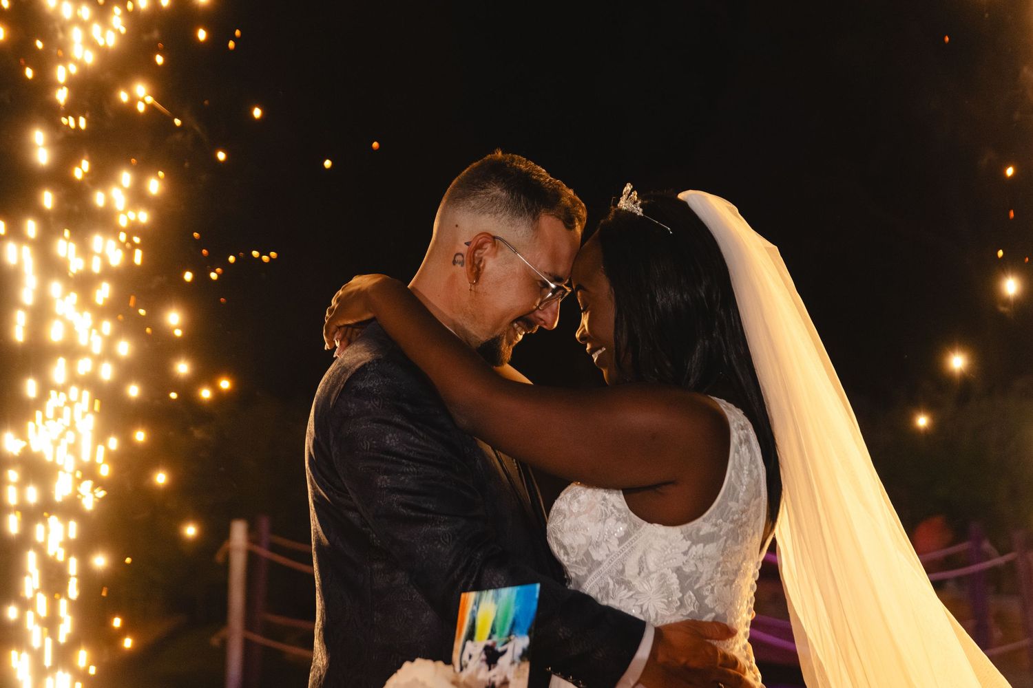 Couple shares intimate moment under cascading sparklers at nighttime wedding reception.