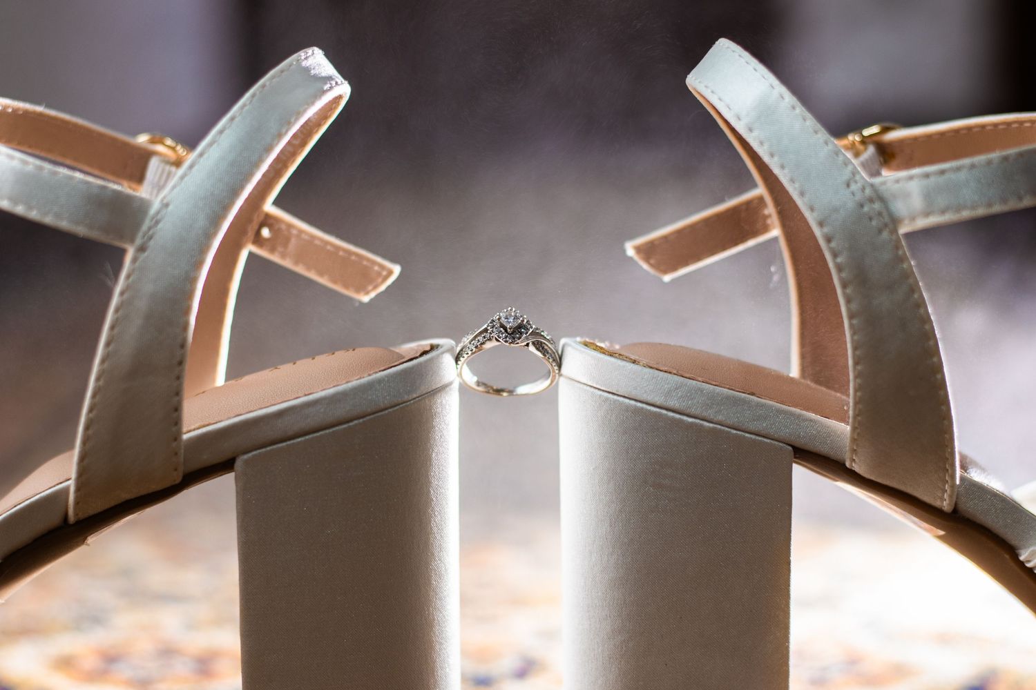 Wedding ring positioned between two silver block heel sandals in artistic detail shot.