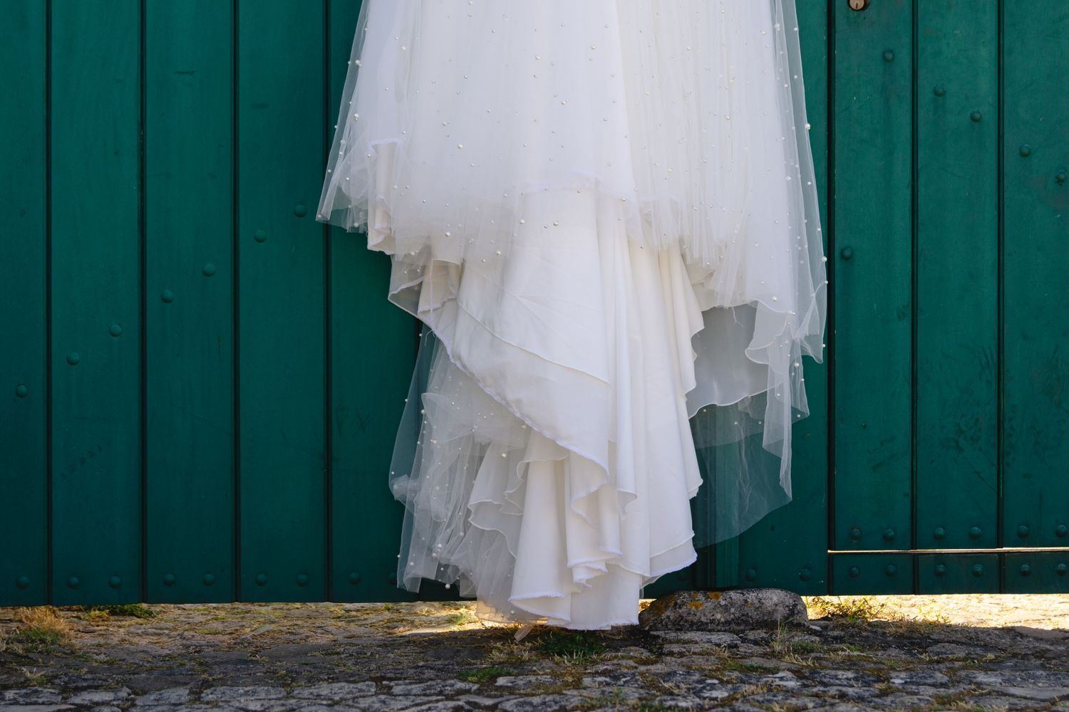 White wedding dresses hanging on hangers against a teal wall.