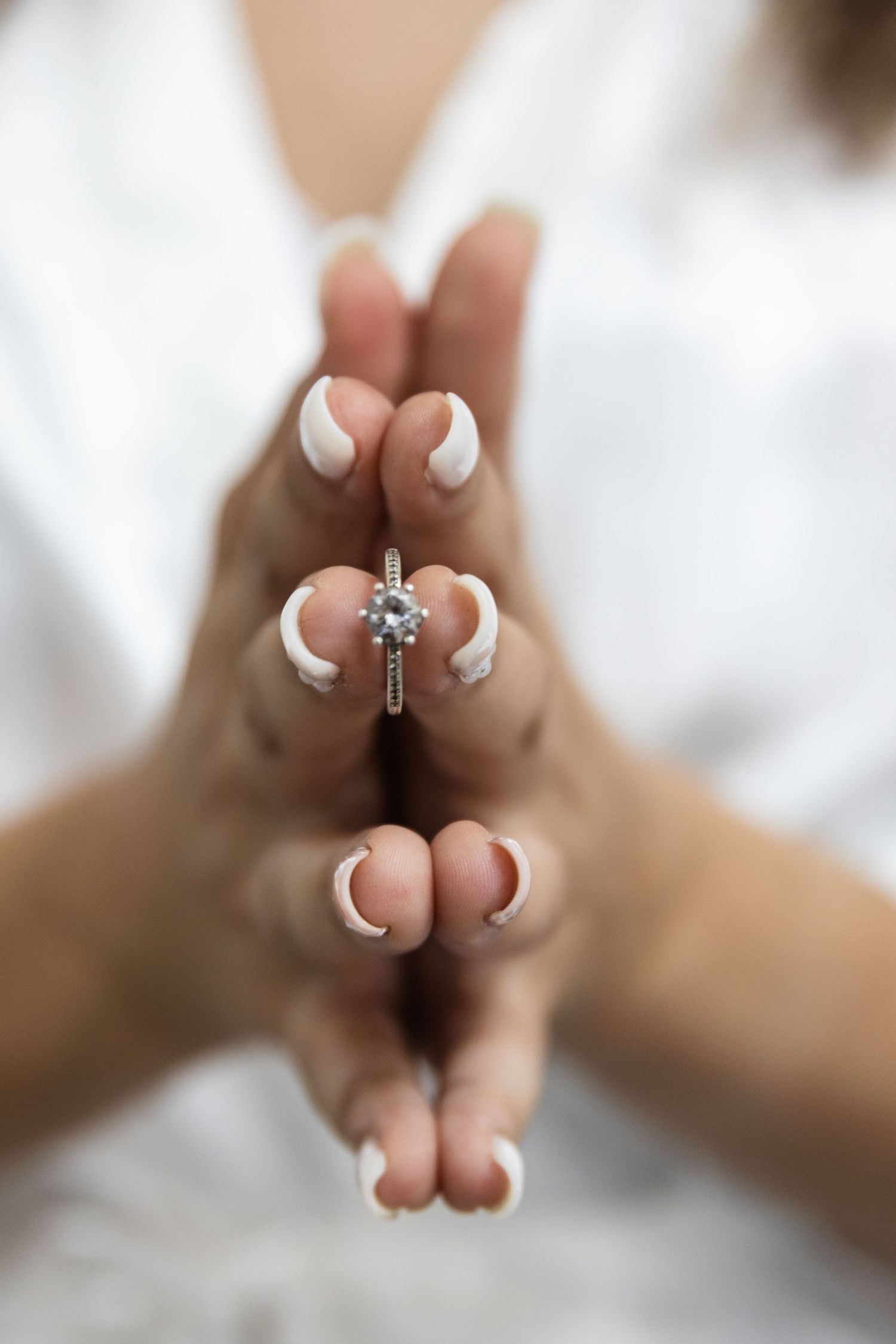 Close-up of manicured hands displaying an engagement ring against a white background.