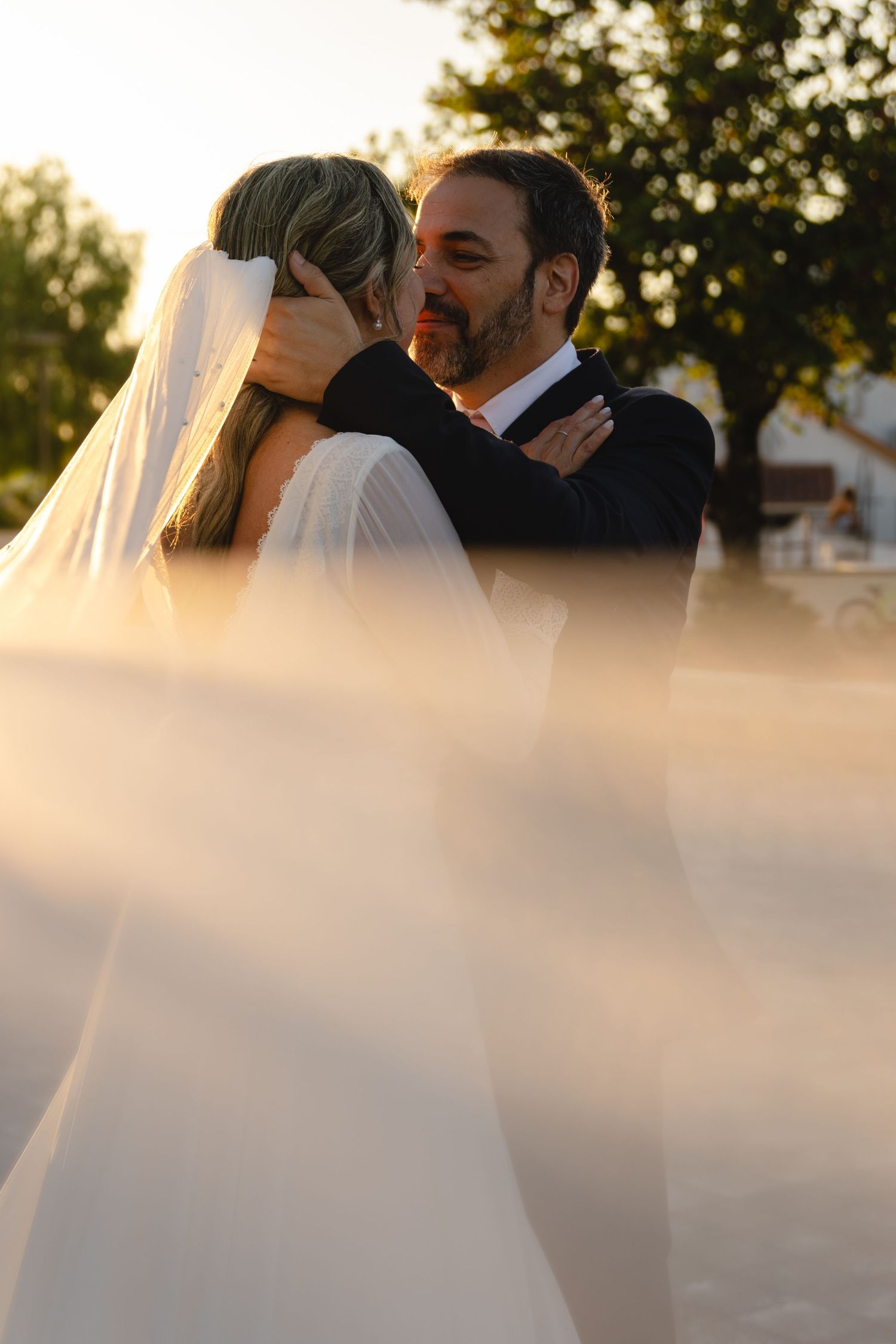An intimate wedding portrait with soft lighting and veil in the foreground.