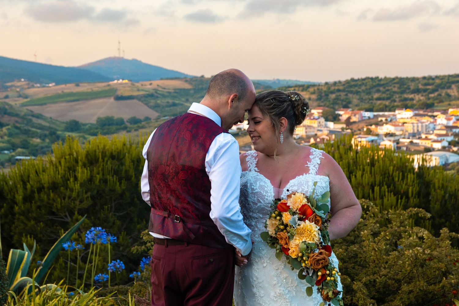 A couple embraces on a hilltop overlooking a scenic mountain landscape.