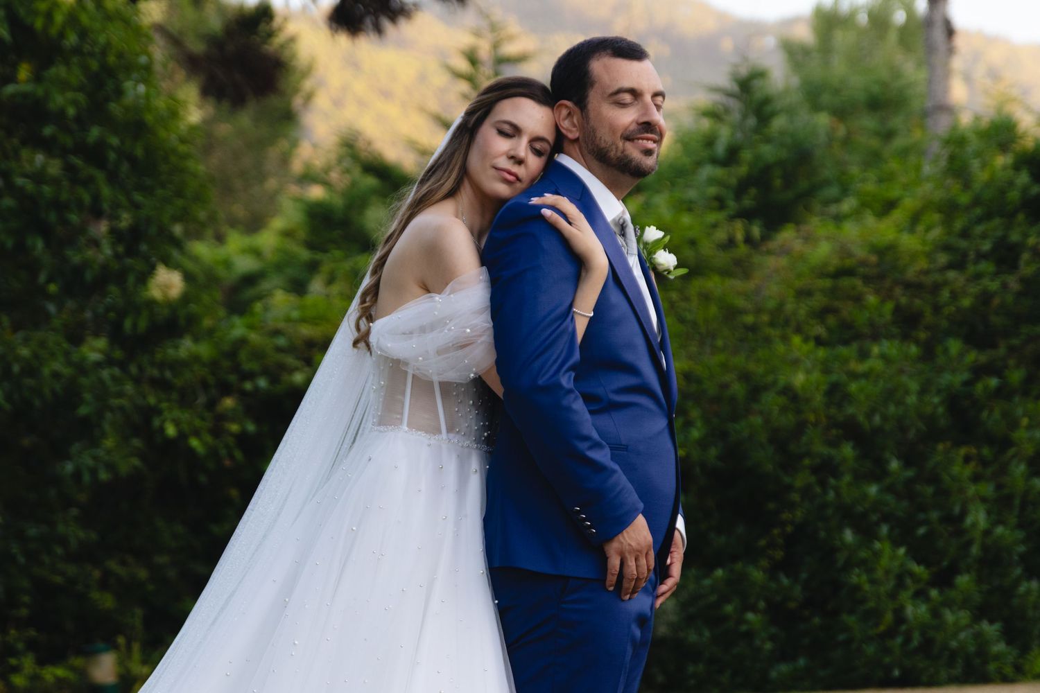 A couple embracing during their outdoor wedding ceremony with greenery in the background.