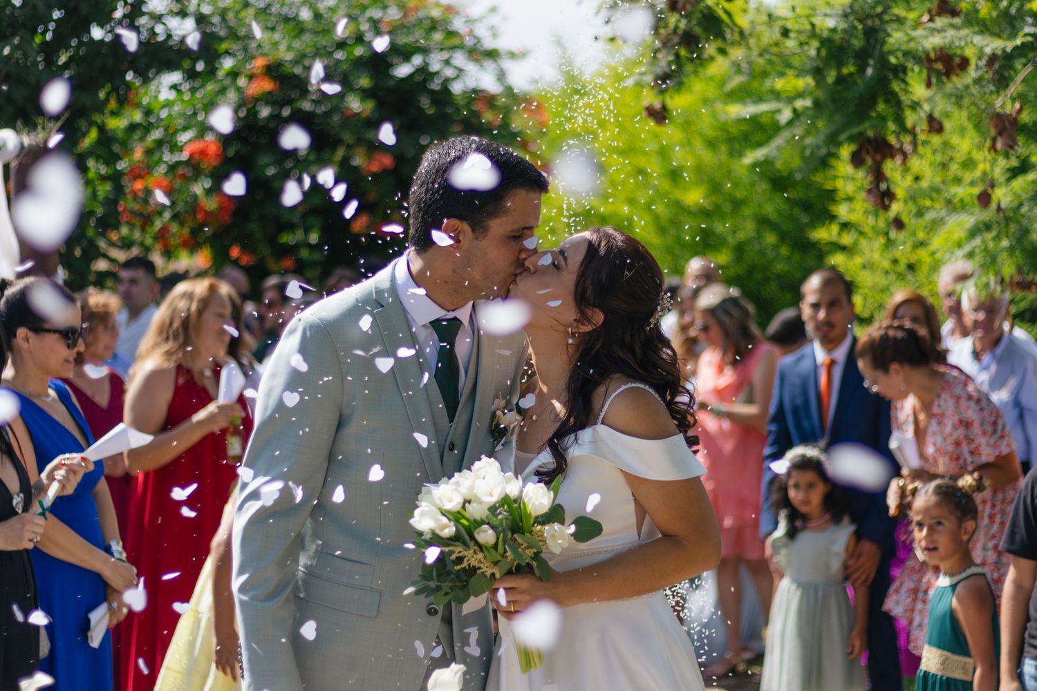 A festive outdoor wedding ceremony with guests throwing white confetti.