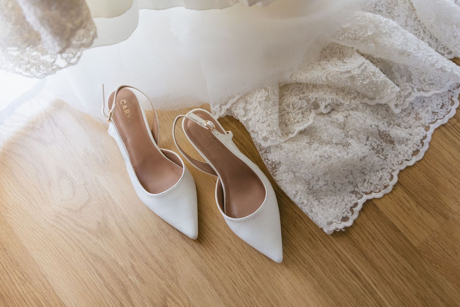 White lace wedding shoes and accessories arranged on wooden floor.