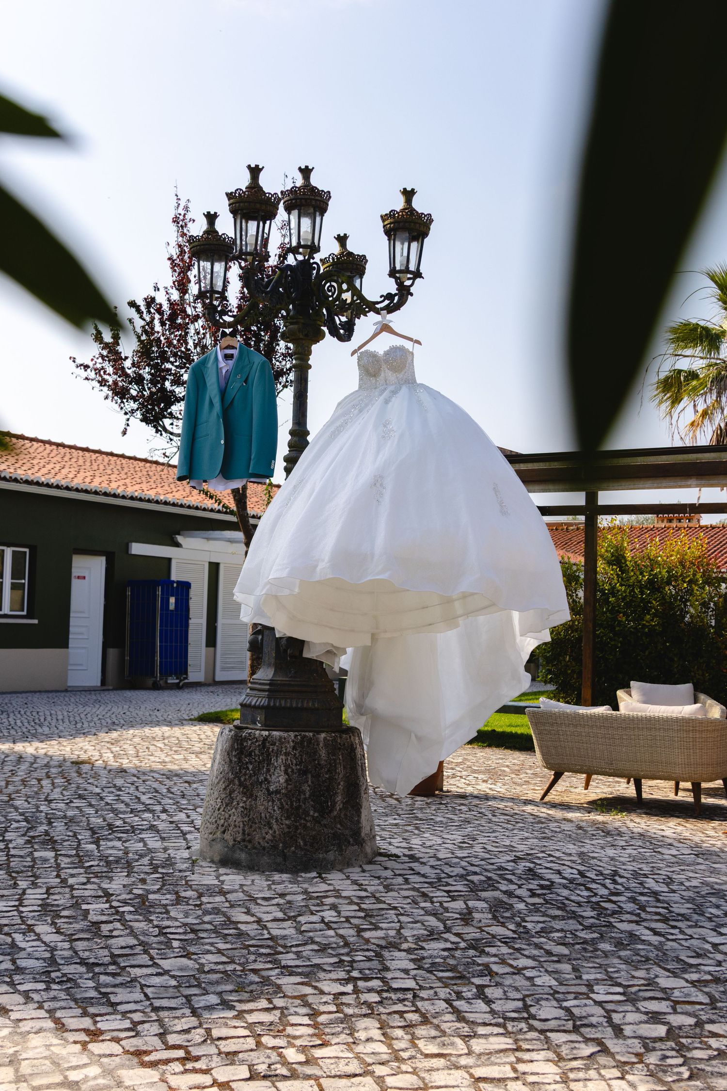 A white wedding dress and turquoise suit hanging on an ornate street lamp post in a cobblestone courtyard.