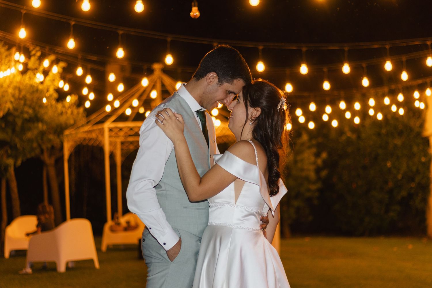 A romantic evening dance under string lights at an outdoor wedding reception.