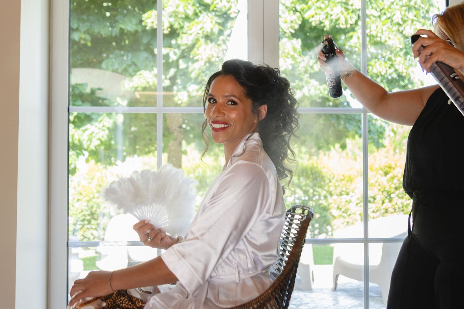 A person getting their hair styled while sitting in a chair and laughing during wedding preparations.